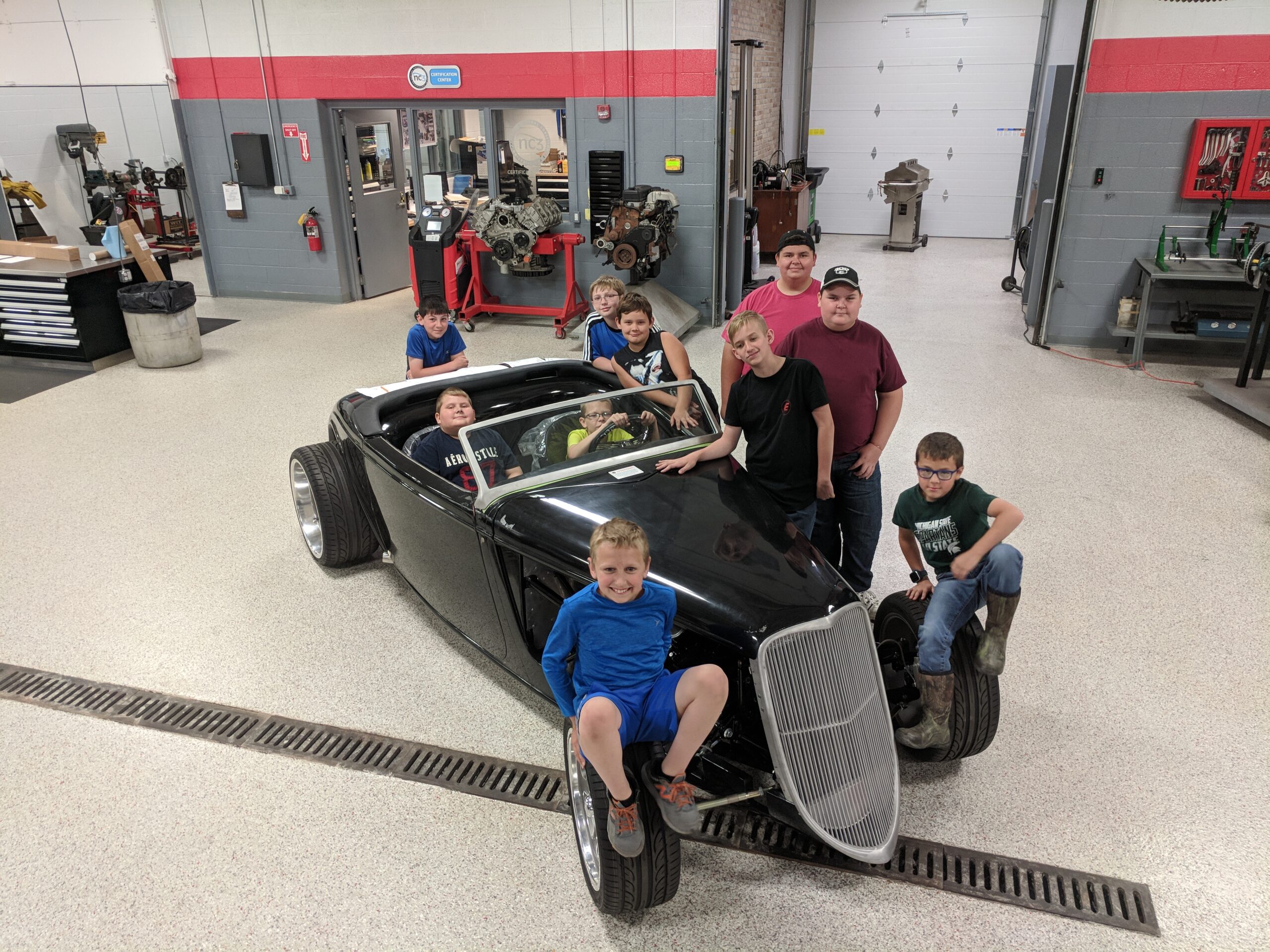 Young students at automotive summer camp sitting on hot rod car